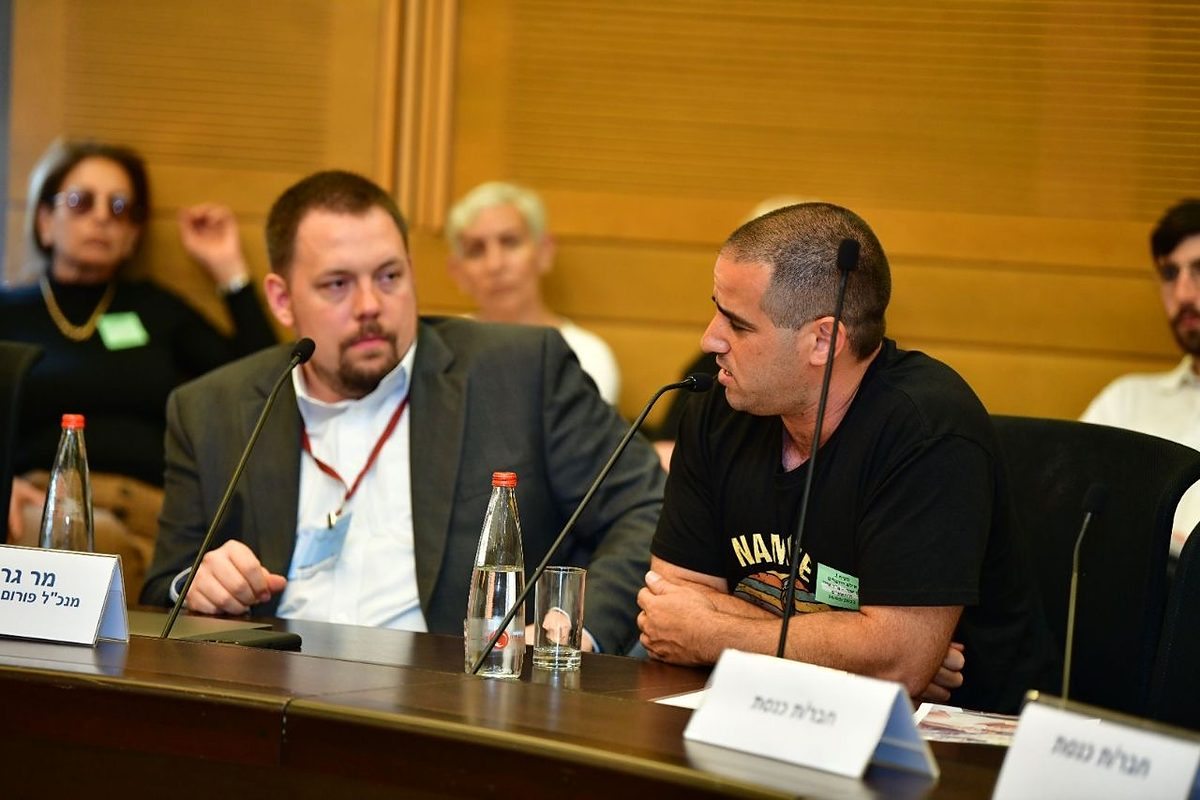Gregg Roman, seated behind his Hebrew name placard at a Knesset committee table, listens as a witness testifies